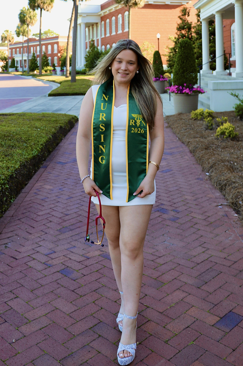 student with a graduation stole in front of campus